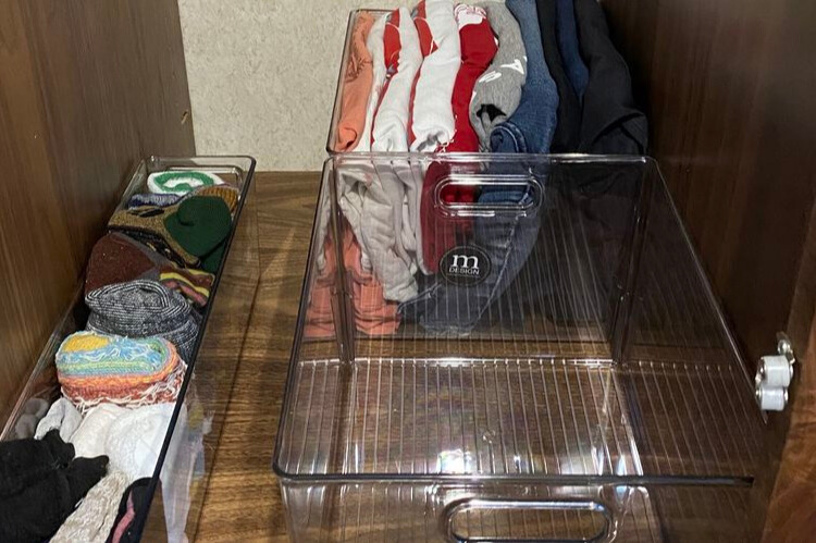 A closeup photo of clothes stored in clear storage bins in a closet.