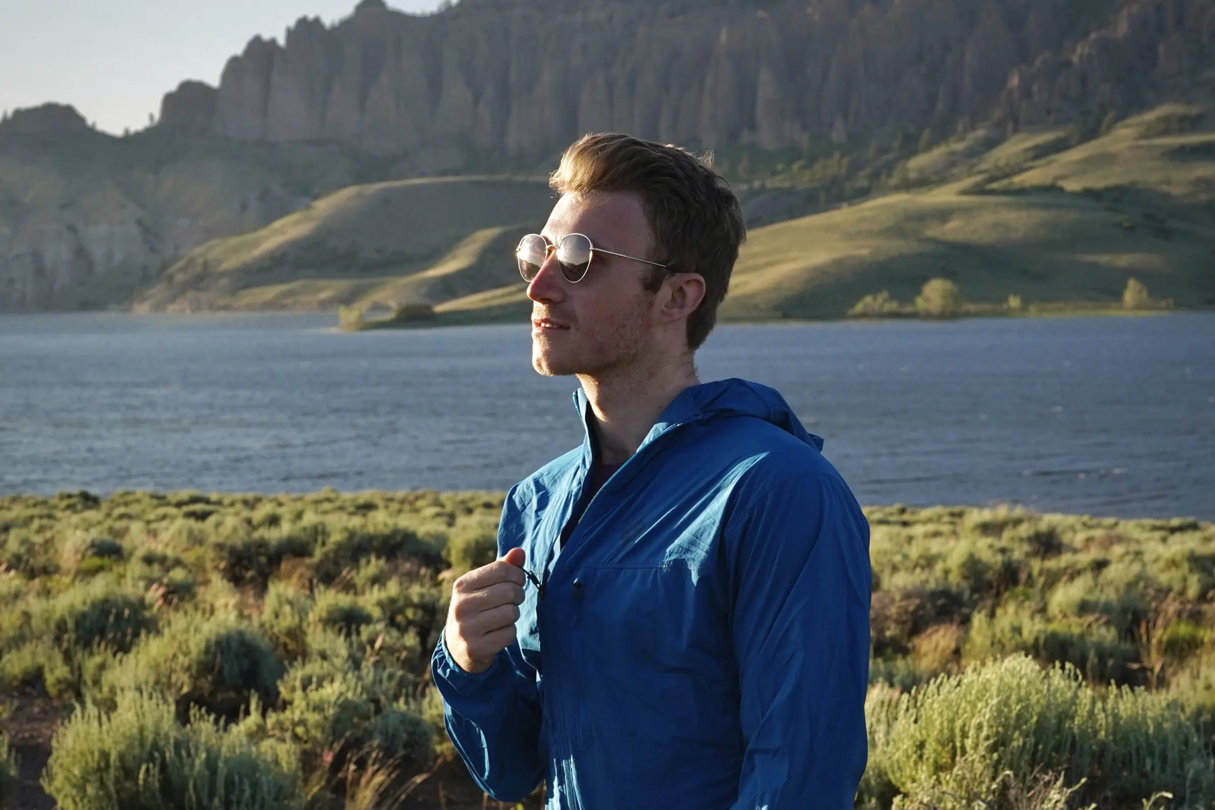 Man stands next to a lake and zips up a windbreaker jacket