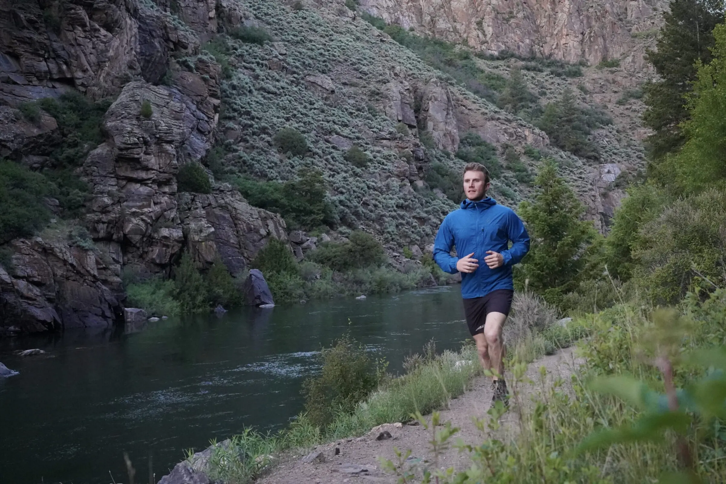 Man runs down a trail wearing a blue windbreaker jacket