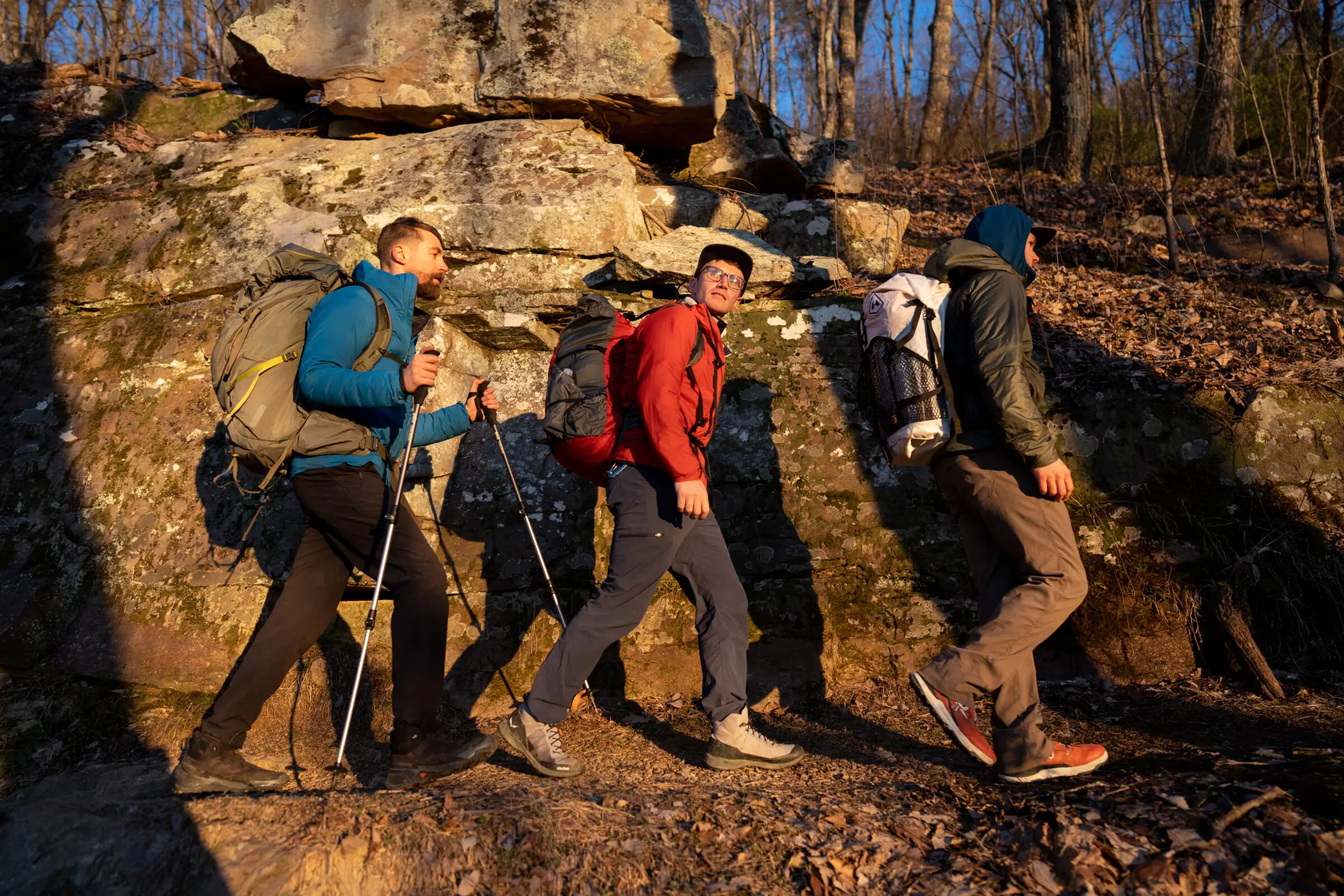 3 men walk down a trail while wearing windbreaker jackets.