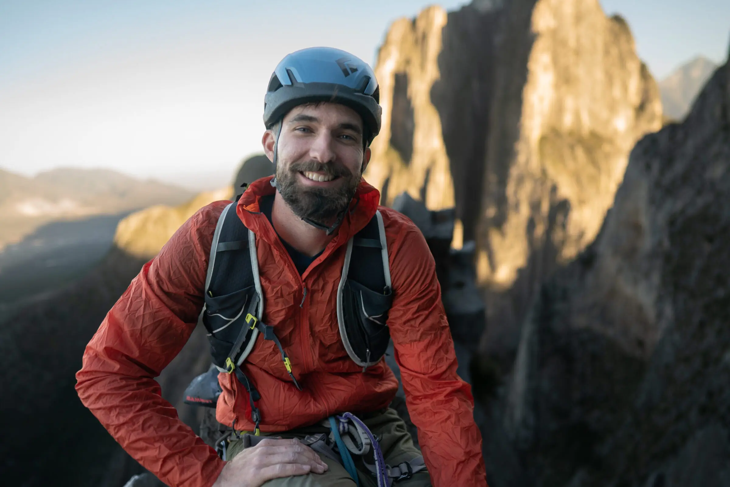 Man smiling on top of a mountain while wearing a windbreaker jacket