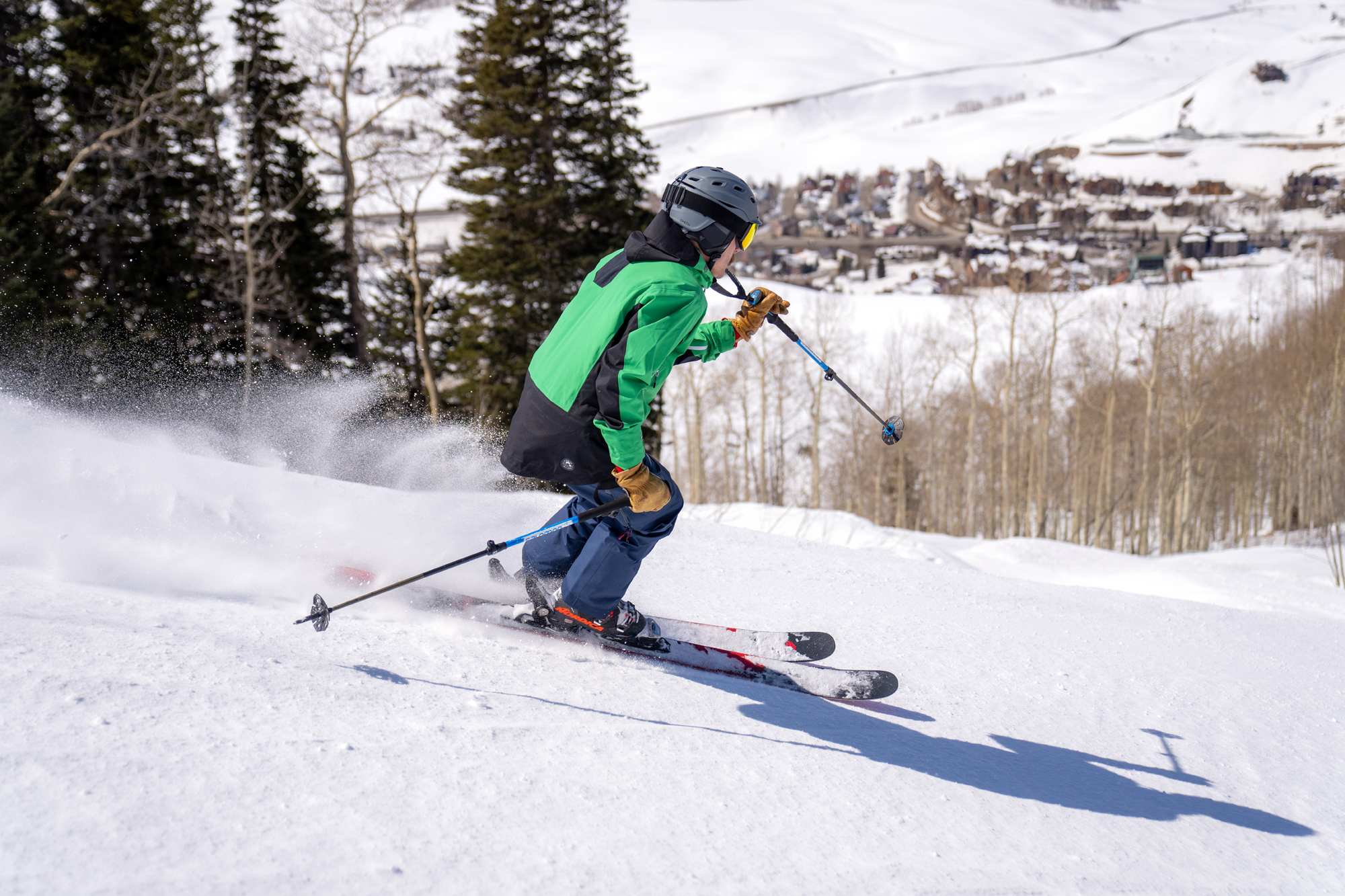 Skier descends groomed slope with town below in the distance