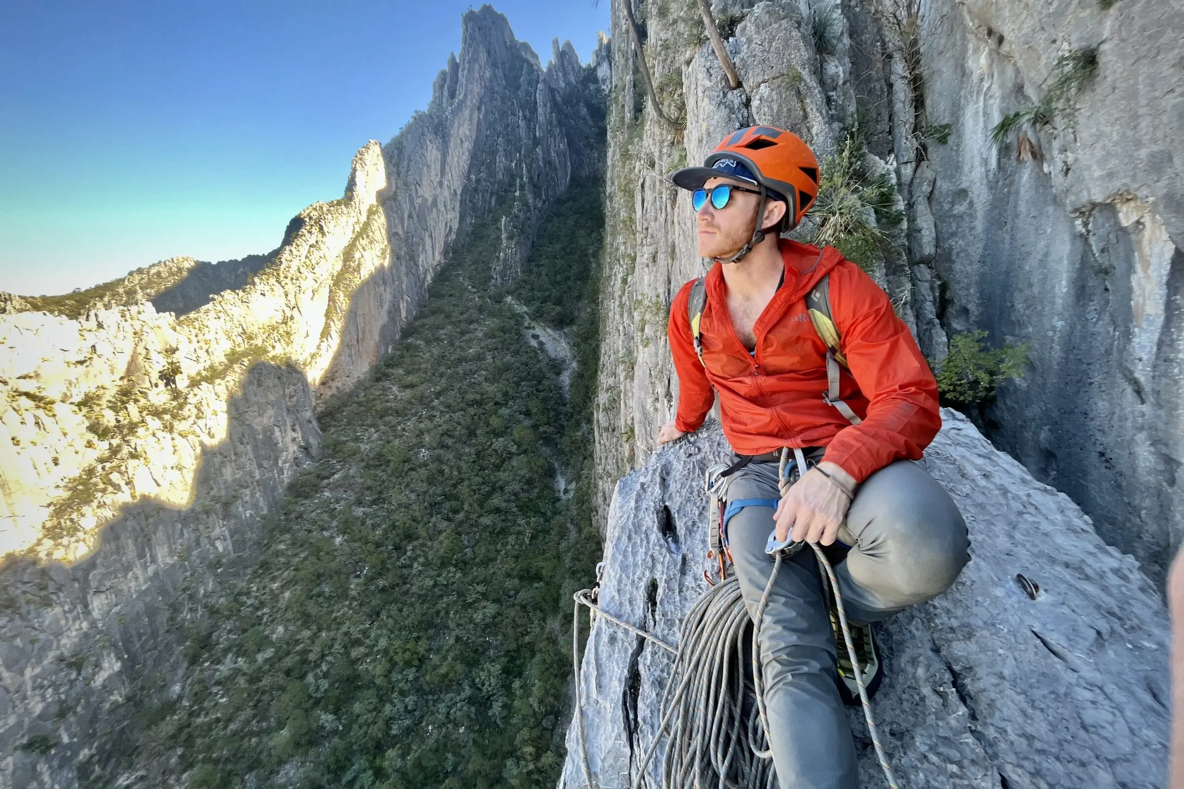 Man sits on top of a mountain while wearing a the Rab Vital Hooded jacket