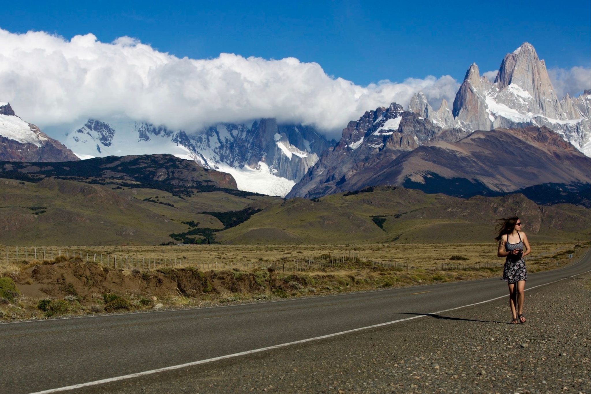woman walks along side of road with mountain in background