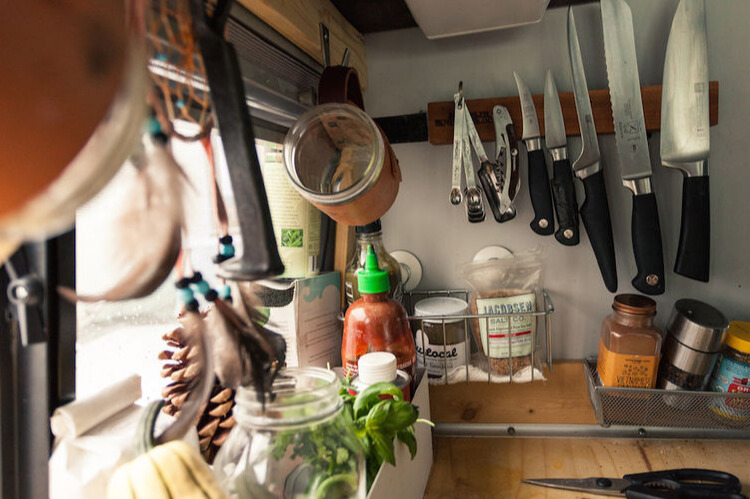 A closeup photo of a camper van kitchen using magnetic wall storage for knives and measuring spoons.