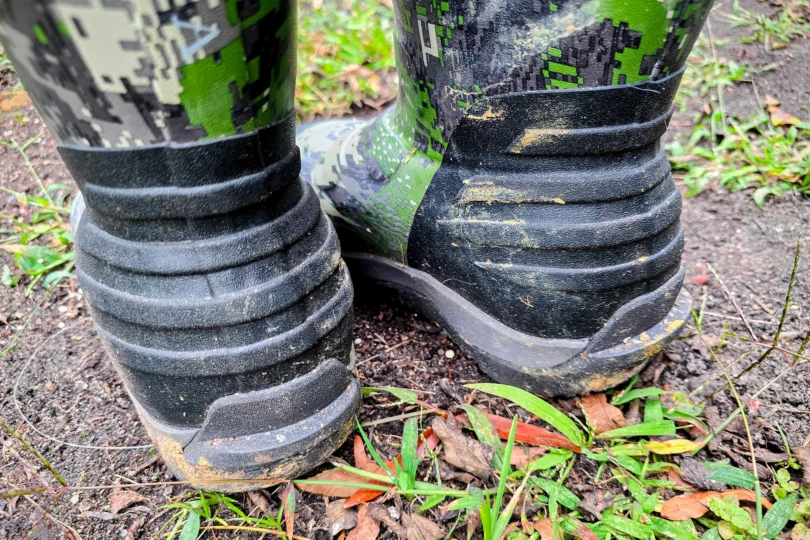 3. Rear view of the boots standing on damp ground, showing textured heel detail