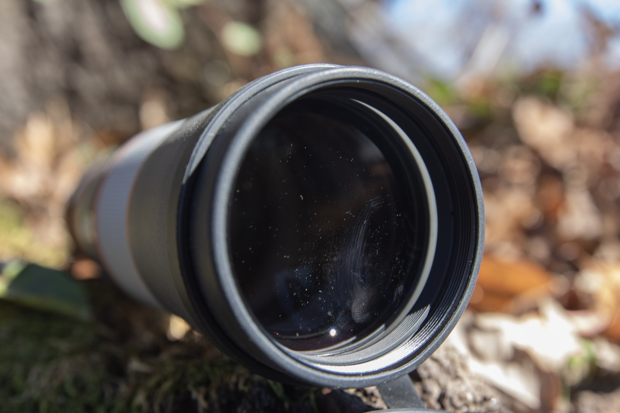 A closeup view of the objective lens of the Maven M.2 Monocular with vegetation in the background.