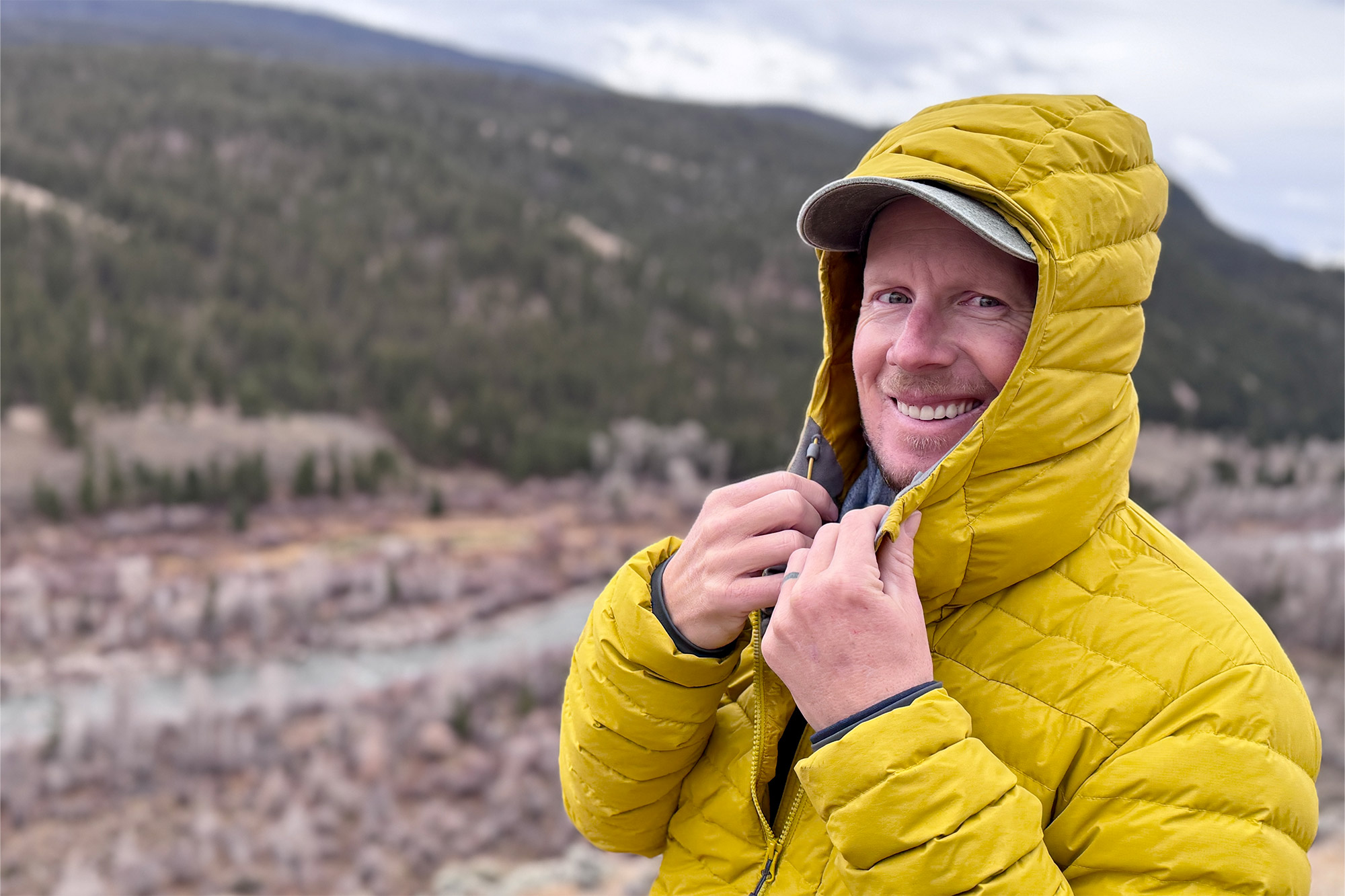 Close-up of a man smiling while zipping up the hood of his yellow Rab Microlight Windstopper Hoody