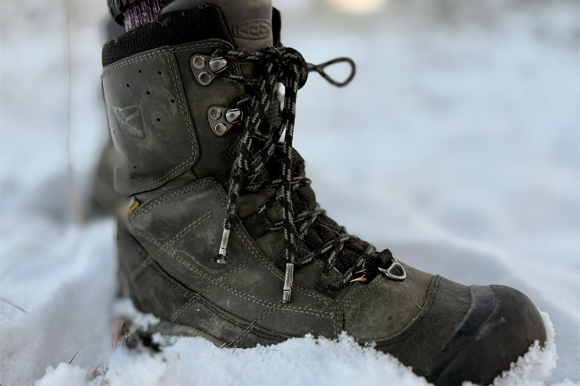 Side view of Revel IV Polar boot in snow, showing durable leather and metal eyelets
