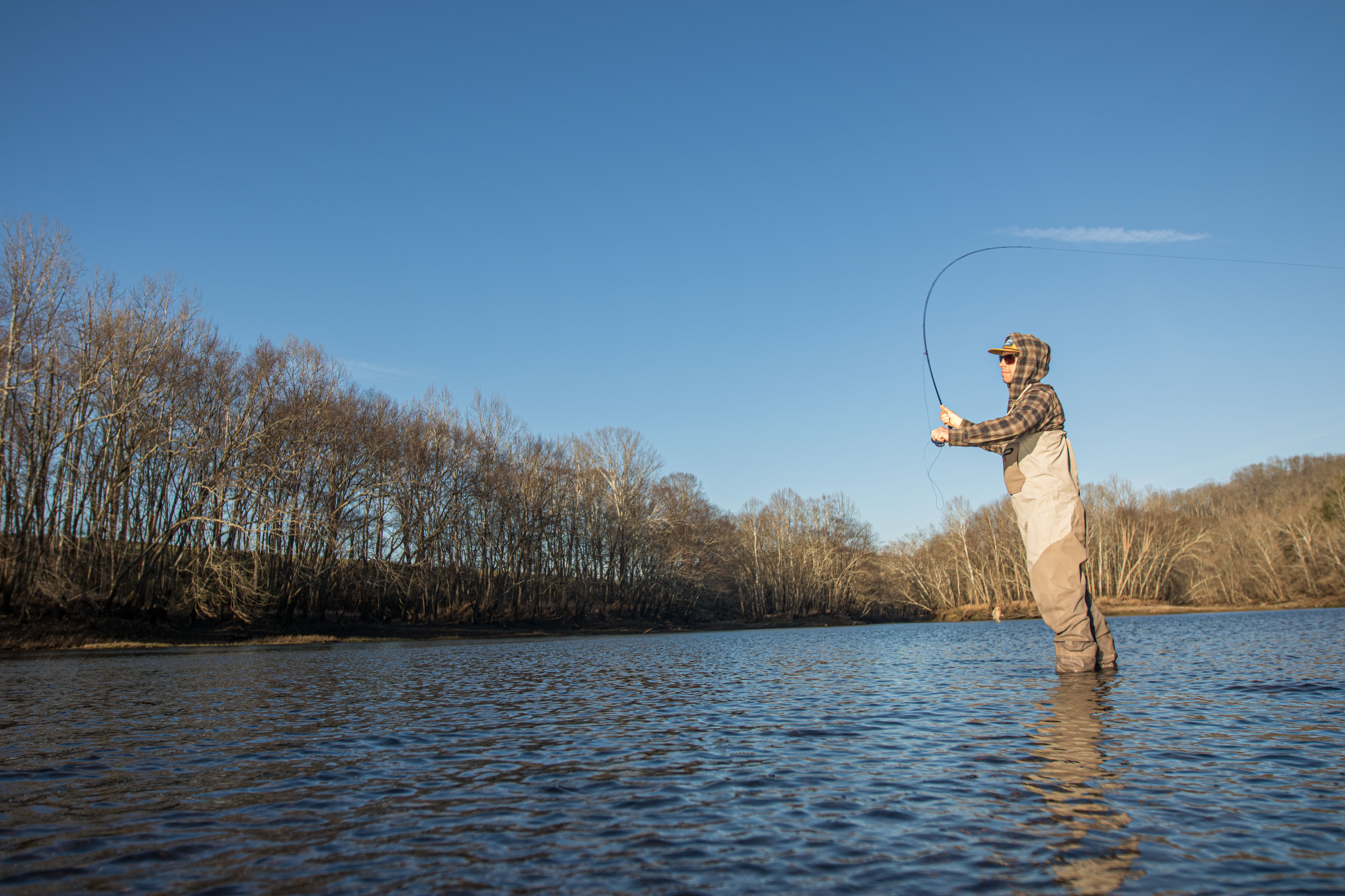 A fly fisherman shin deep in a river casting a fly rod.