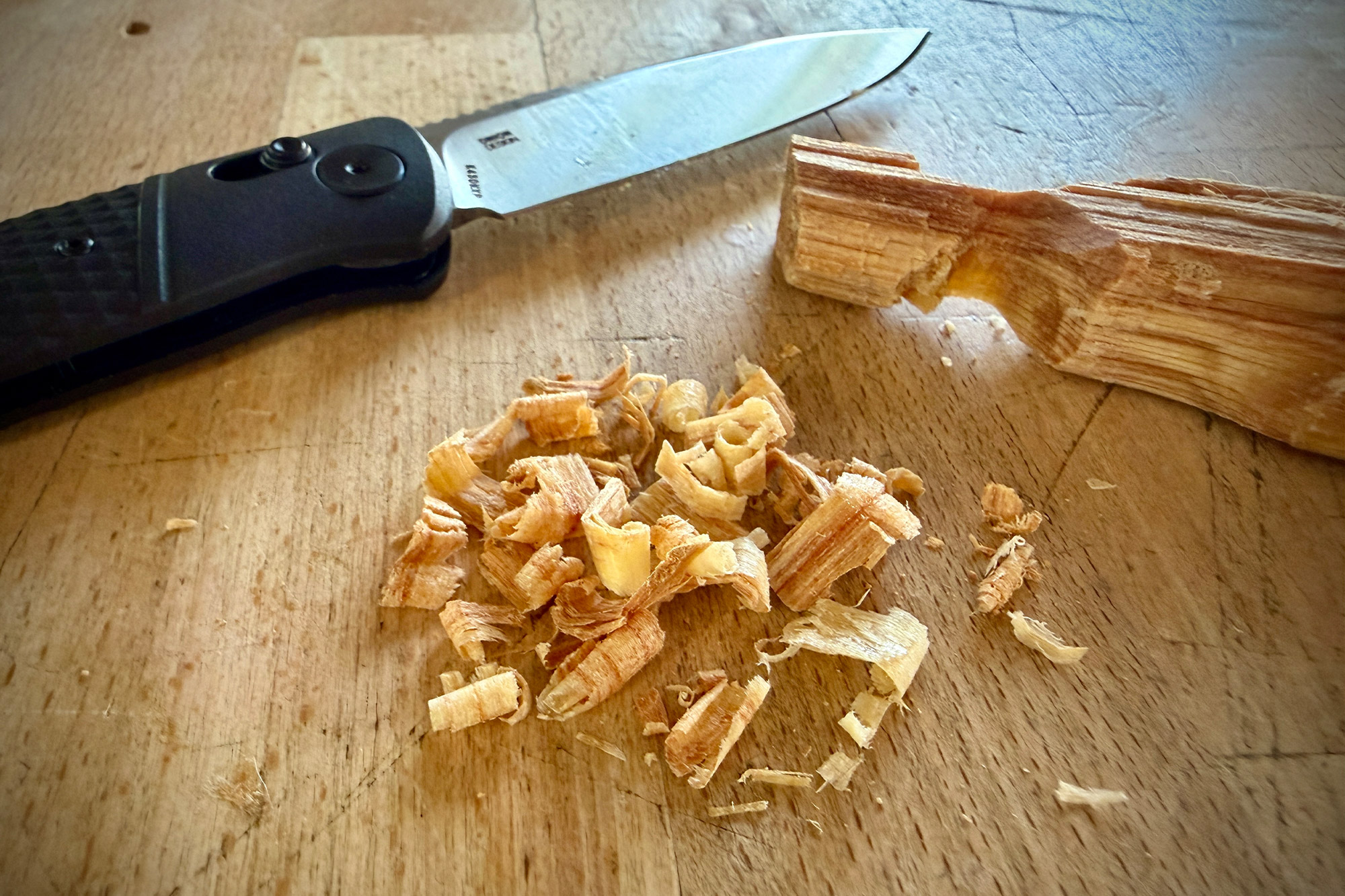 The knife blade resting on a table next to wood shavings and a small split piece of wood