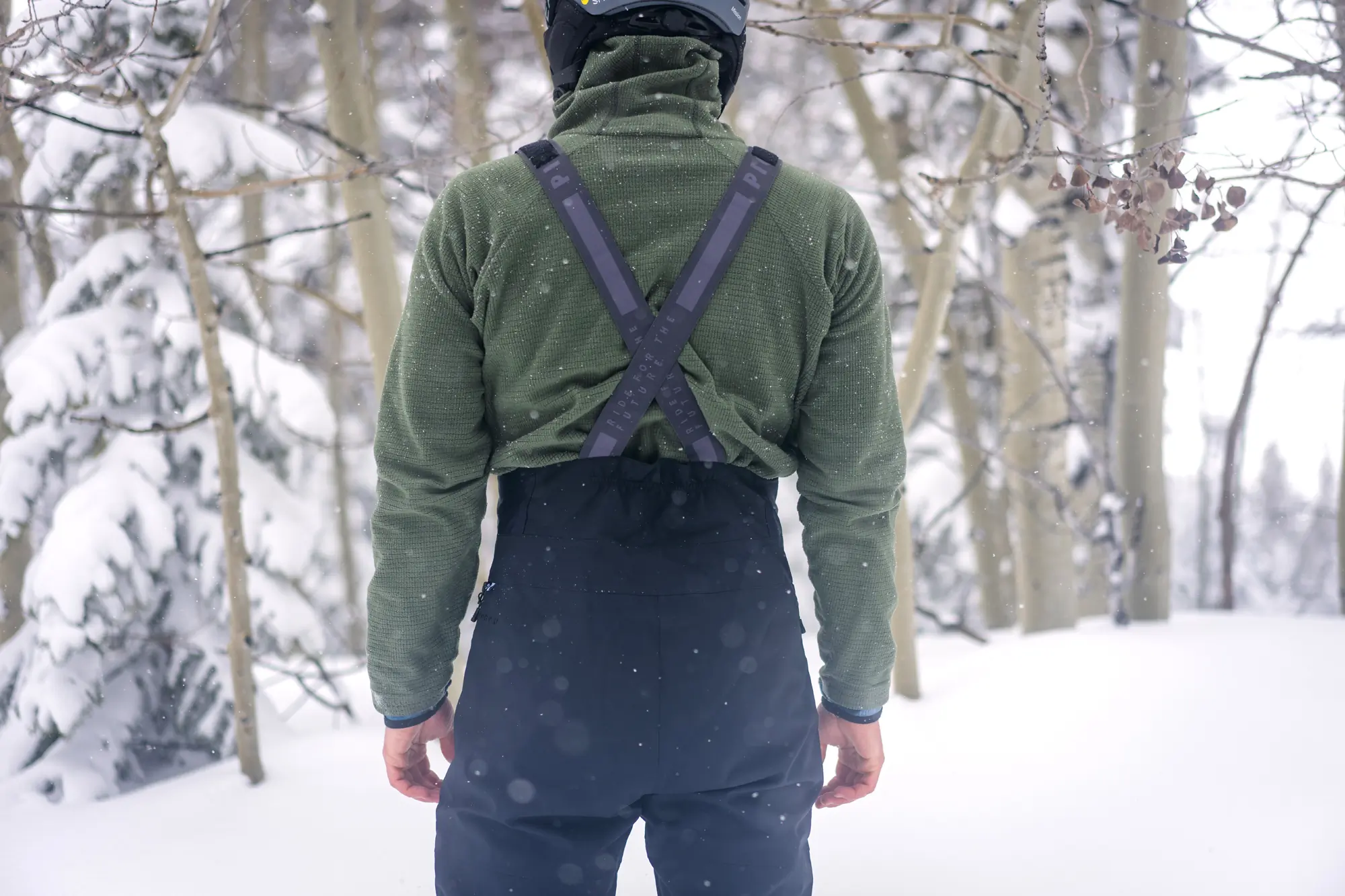 man facing away from camera with ski bibs and fleece midlayer on 