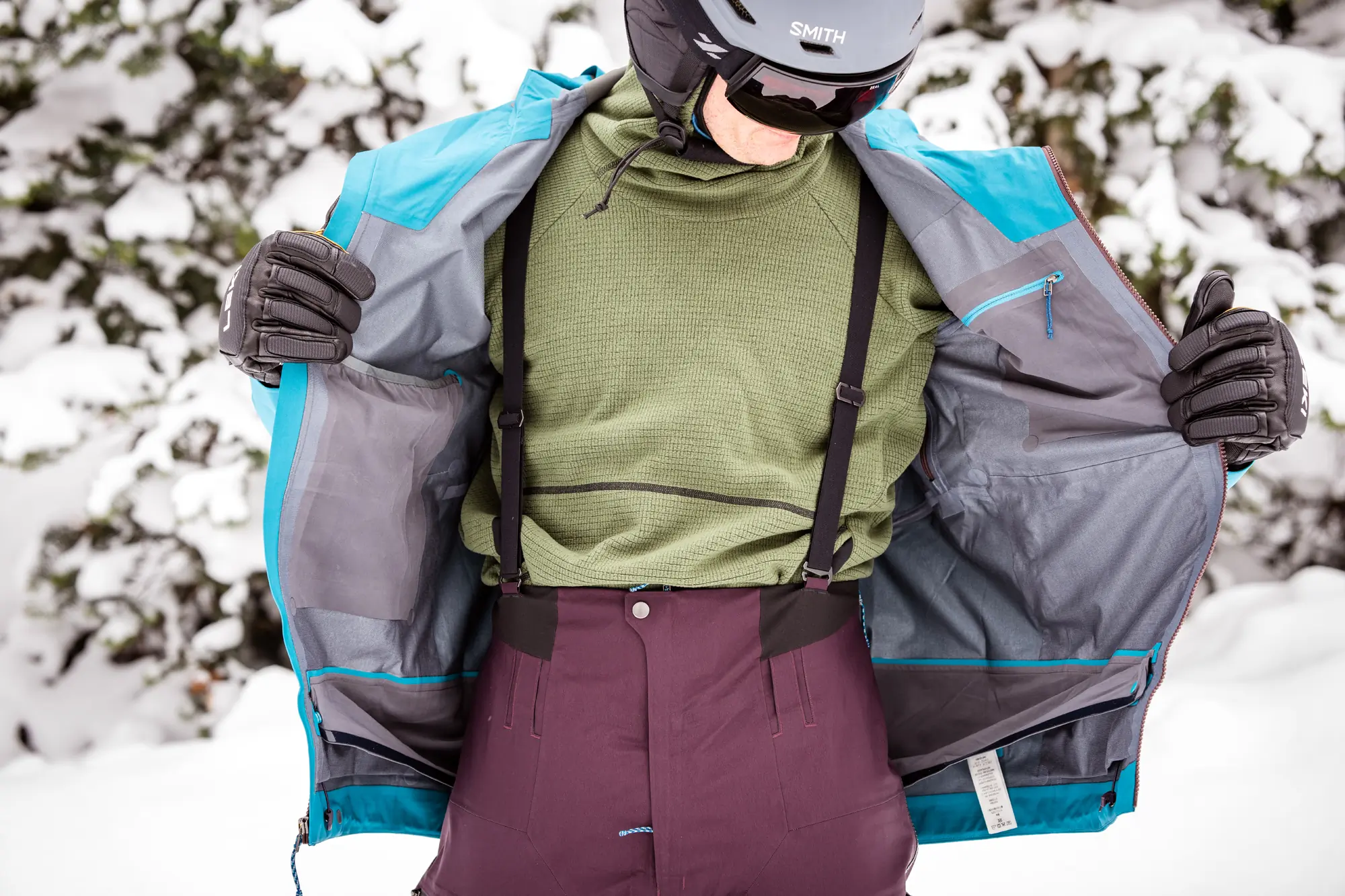 man opening ski jacket and showing snow bibs 
