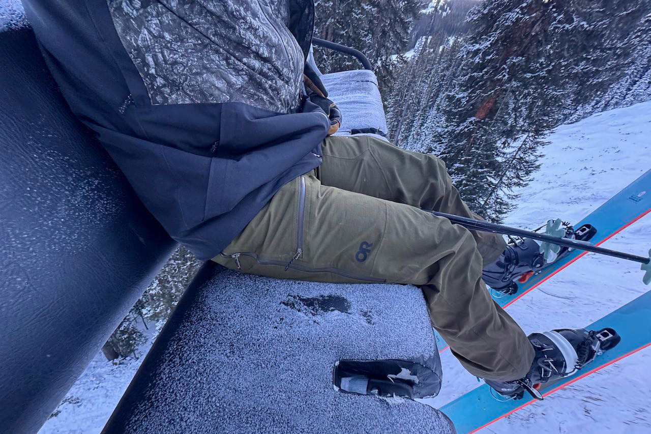 The Powderverse pants are worn while sitting on a ski lift in winter conditions