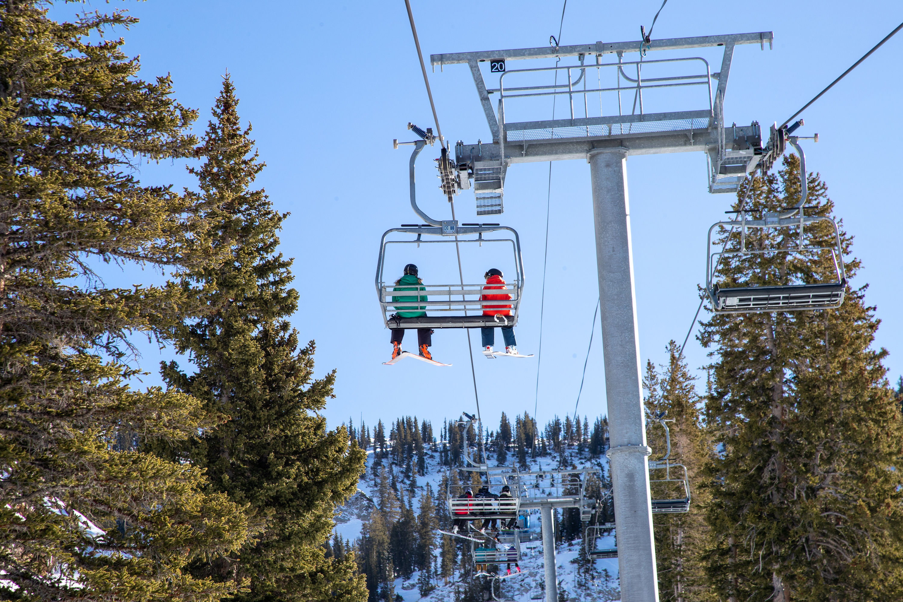 two skiers on a 3 person chairlift on a sunny day