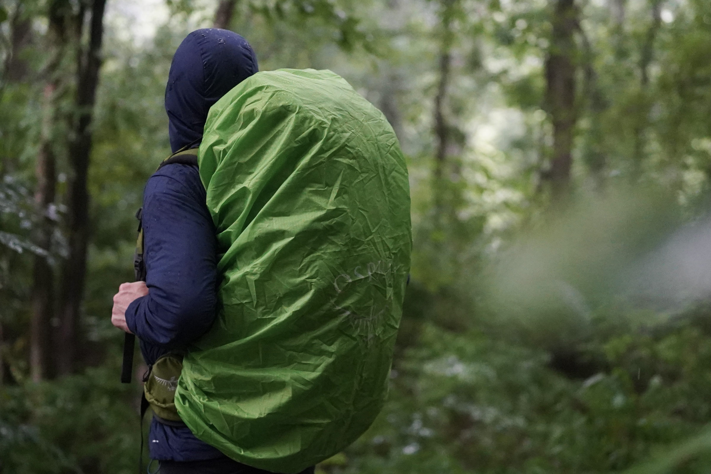 a backpacker uses a backpack with a green osprey rain cover over it