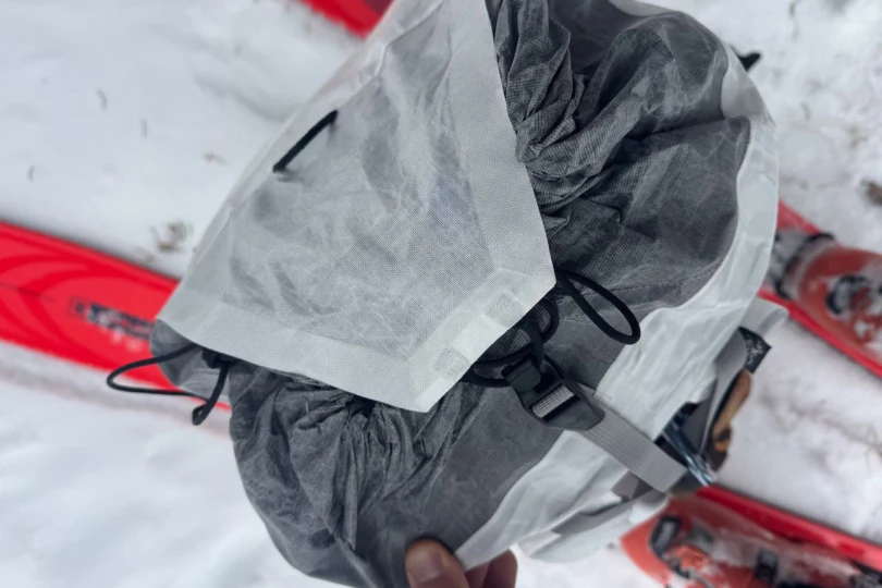 The Alpha SL pack drawcord opening and top flap during a snowy ski tour