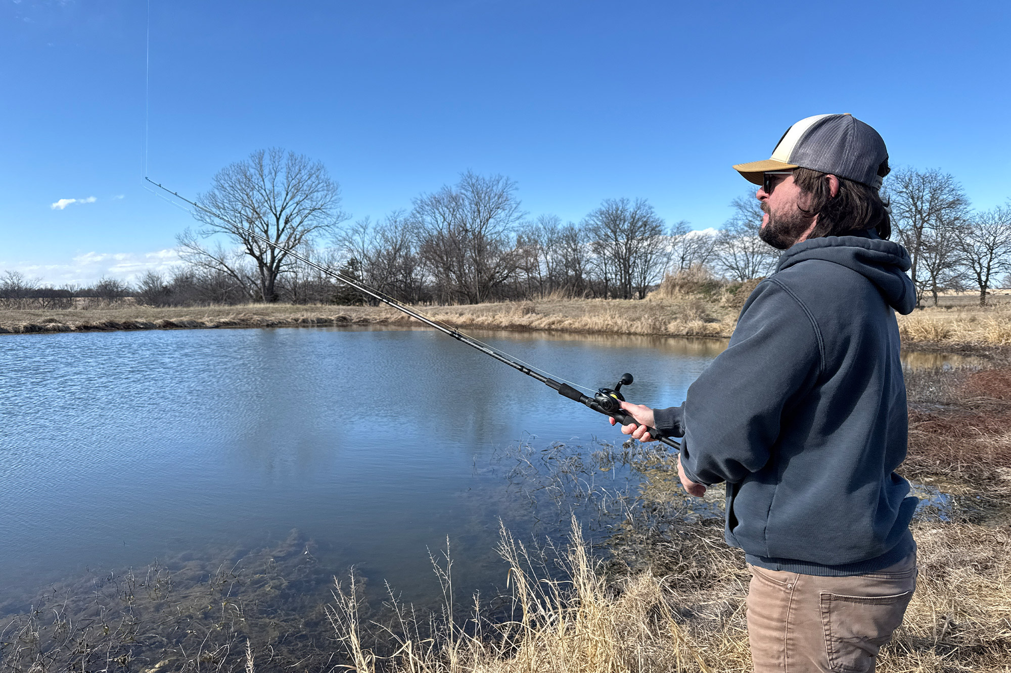 The Beast baitcasting combo is used from the shoreline of a calm pond on a clear day