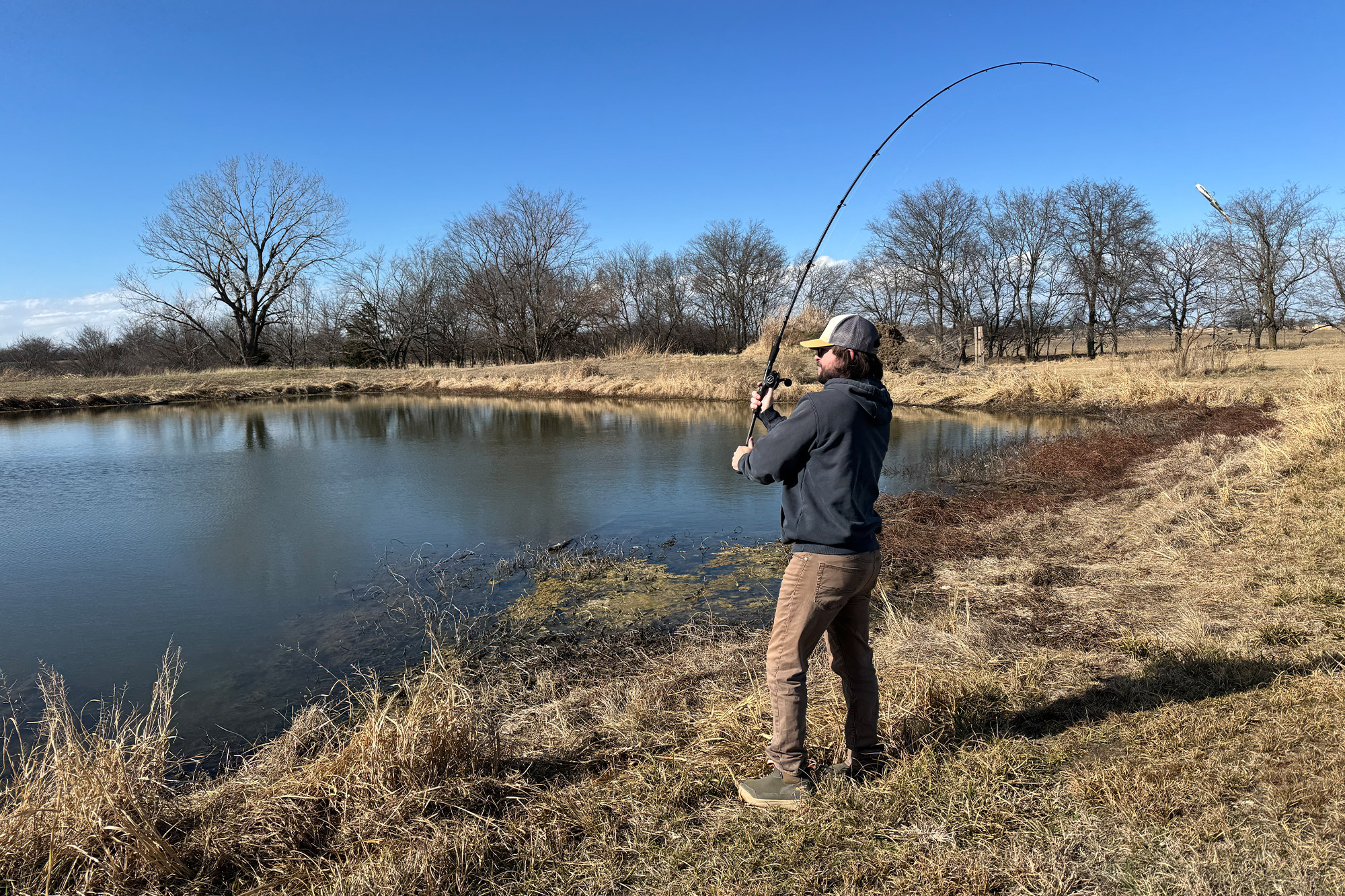 An angler fights a fish with the Beast rod and reel combo bent over a small pond