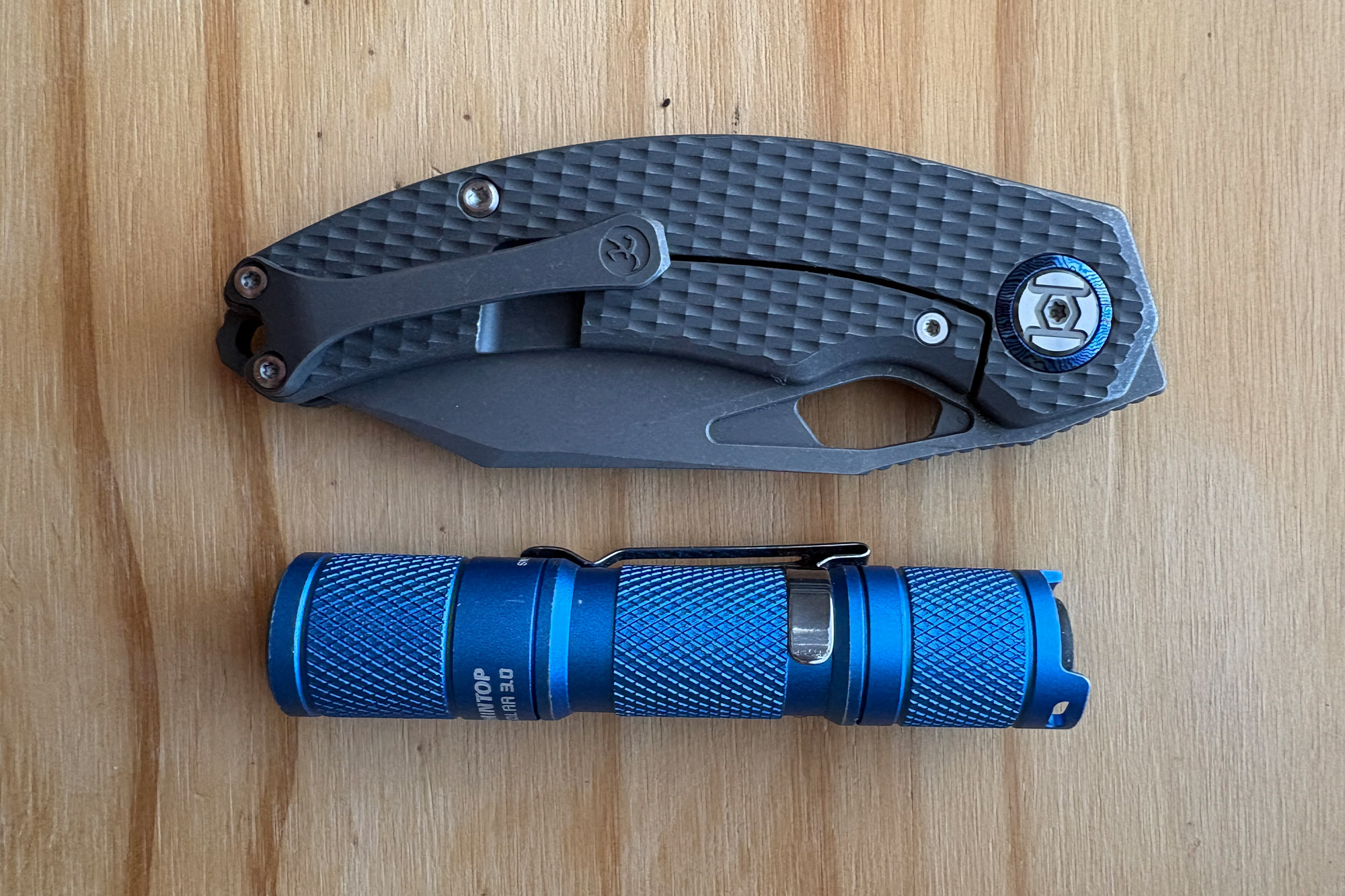 Closed Compadre knife placed above a blue flashlight for size reference