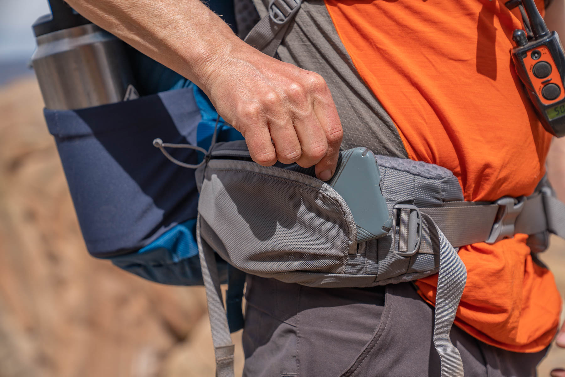 A backpacker pulls a phone out of a hipbelt pocket. 
