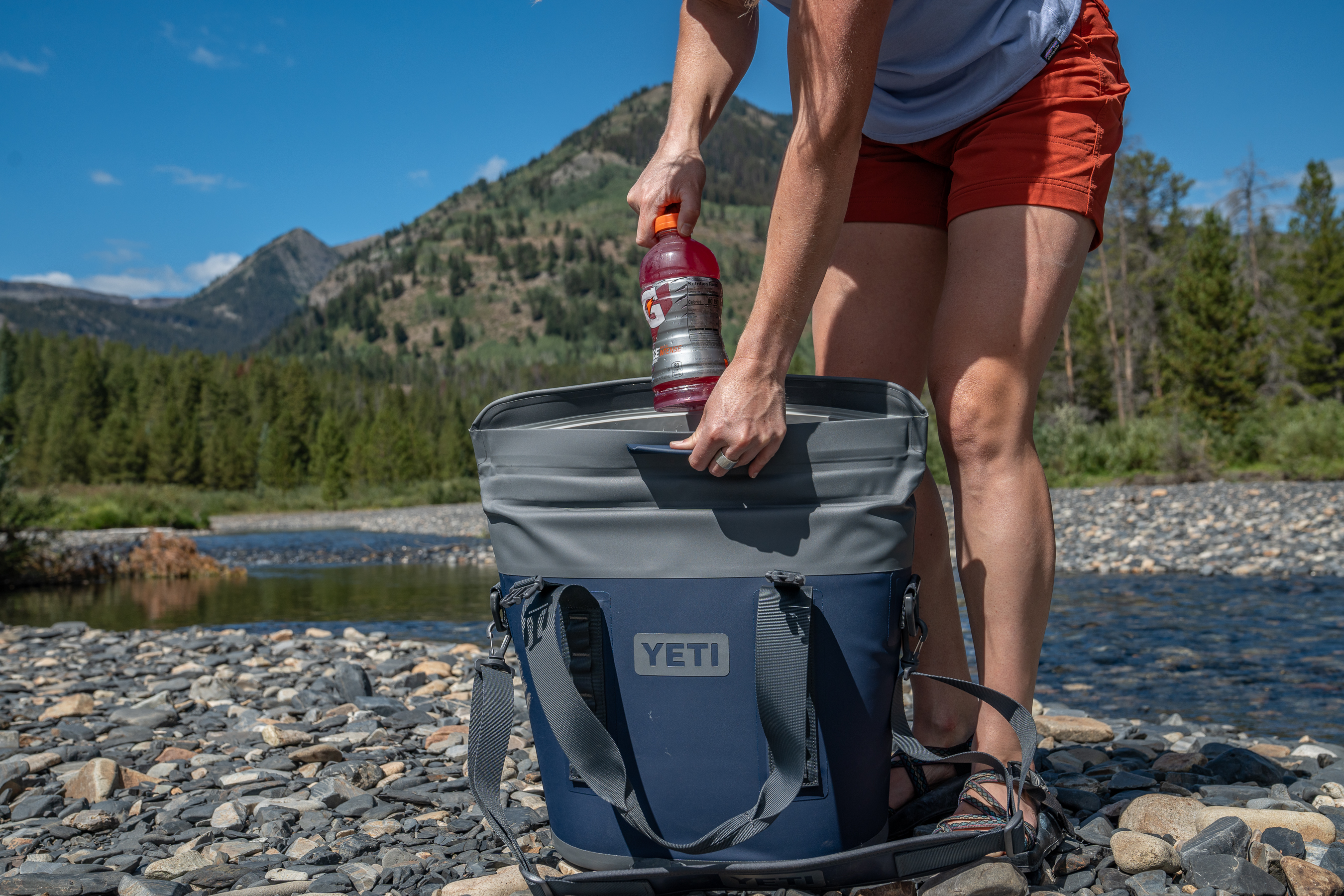 woman pulling beverage out of YETI soft cooler on river bank 