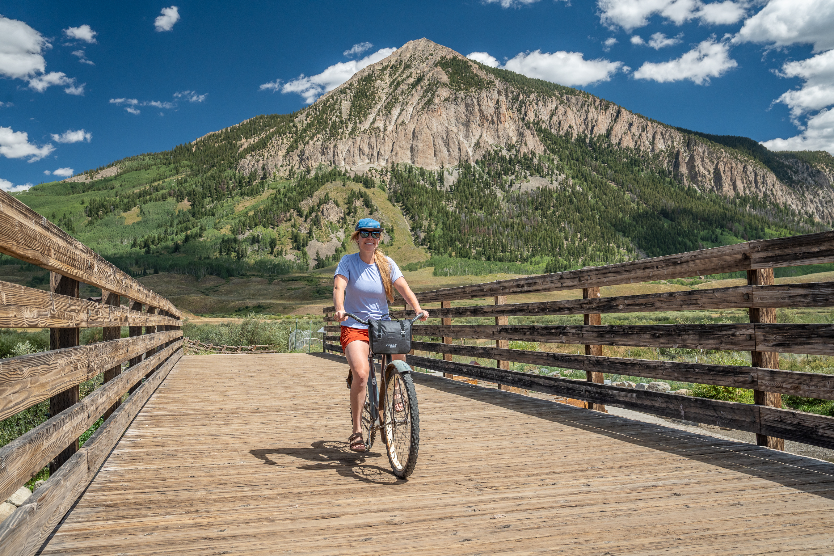 woman riding cruiser bike across bridge with soft cooler attached to handlebars 
