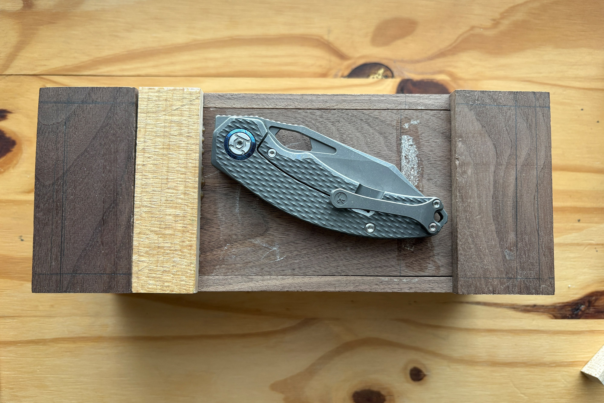 Closed Kunwu knife resting on a wooden jig with different wood tones