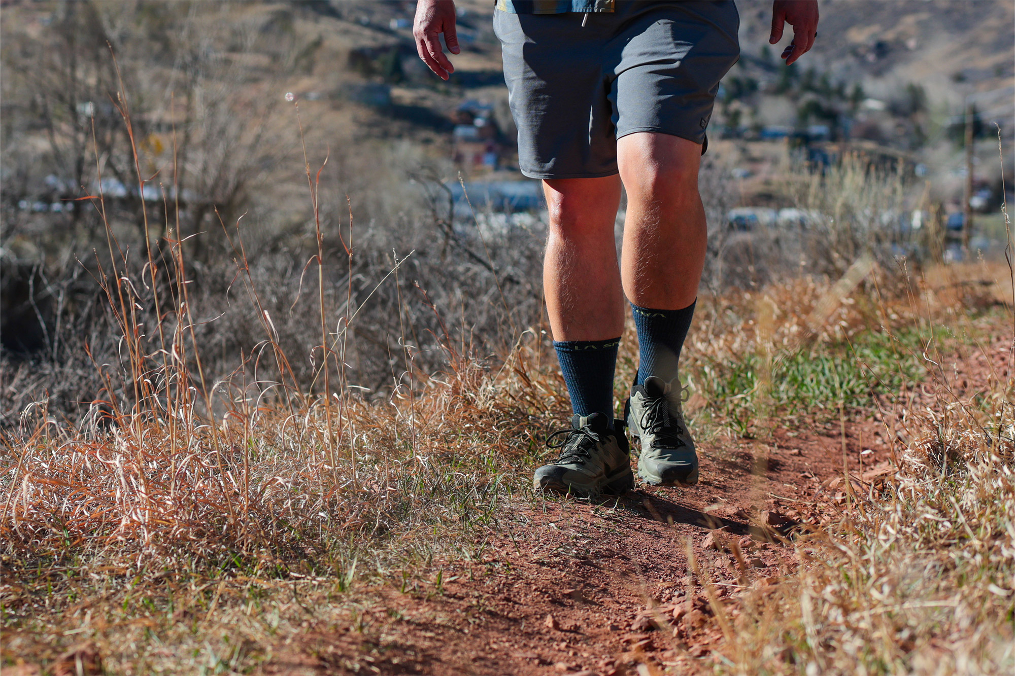 Lower body walking on dirt trail showing trail shoes in motion