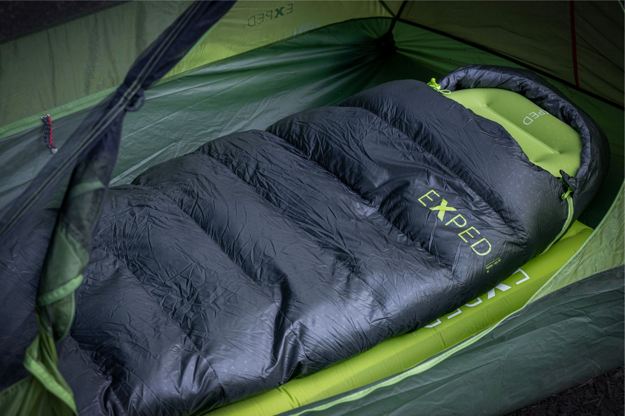 black and green sleeping bag set up in a tent