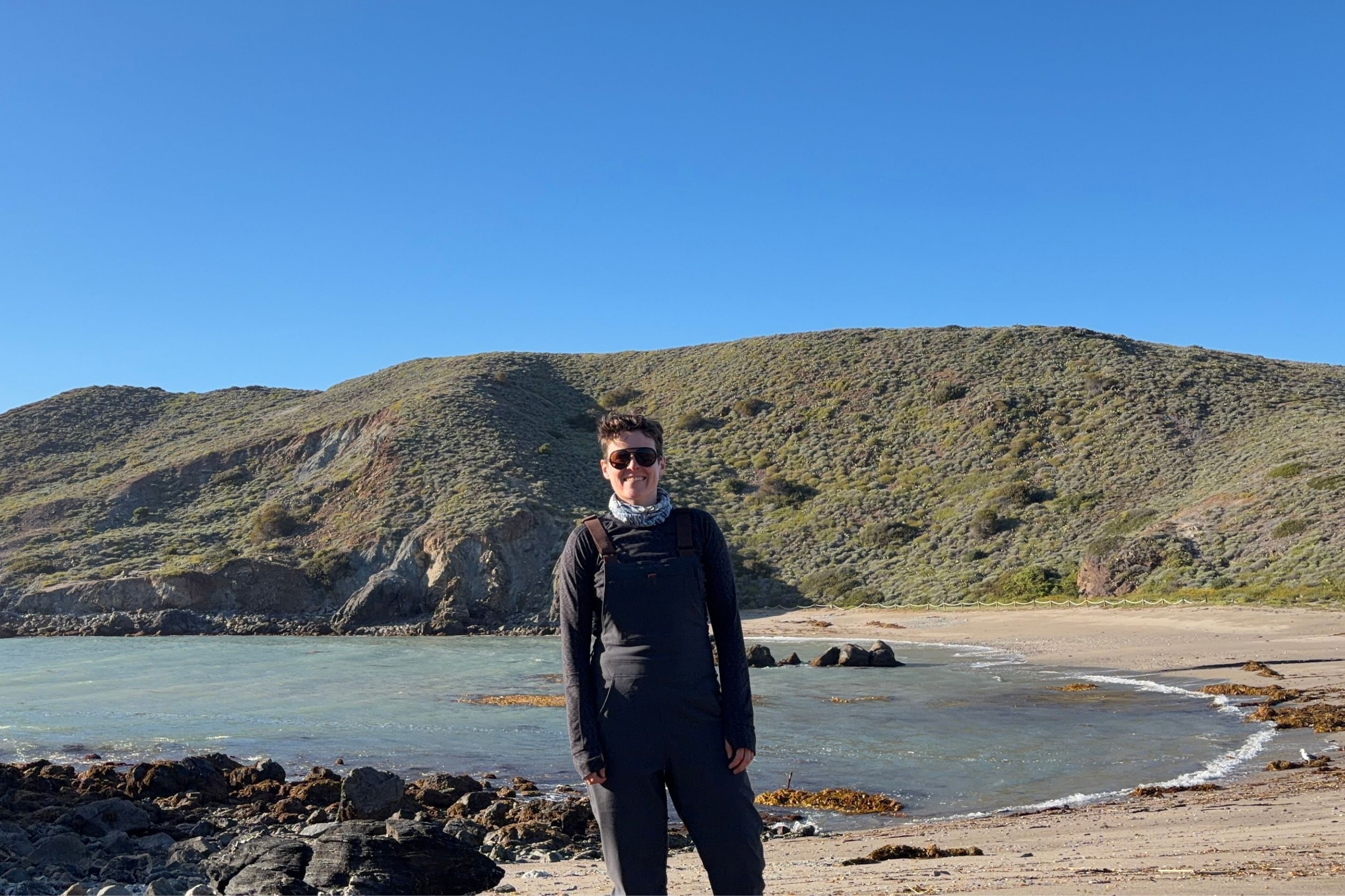 person wears overalls in front of a beach