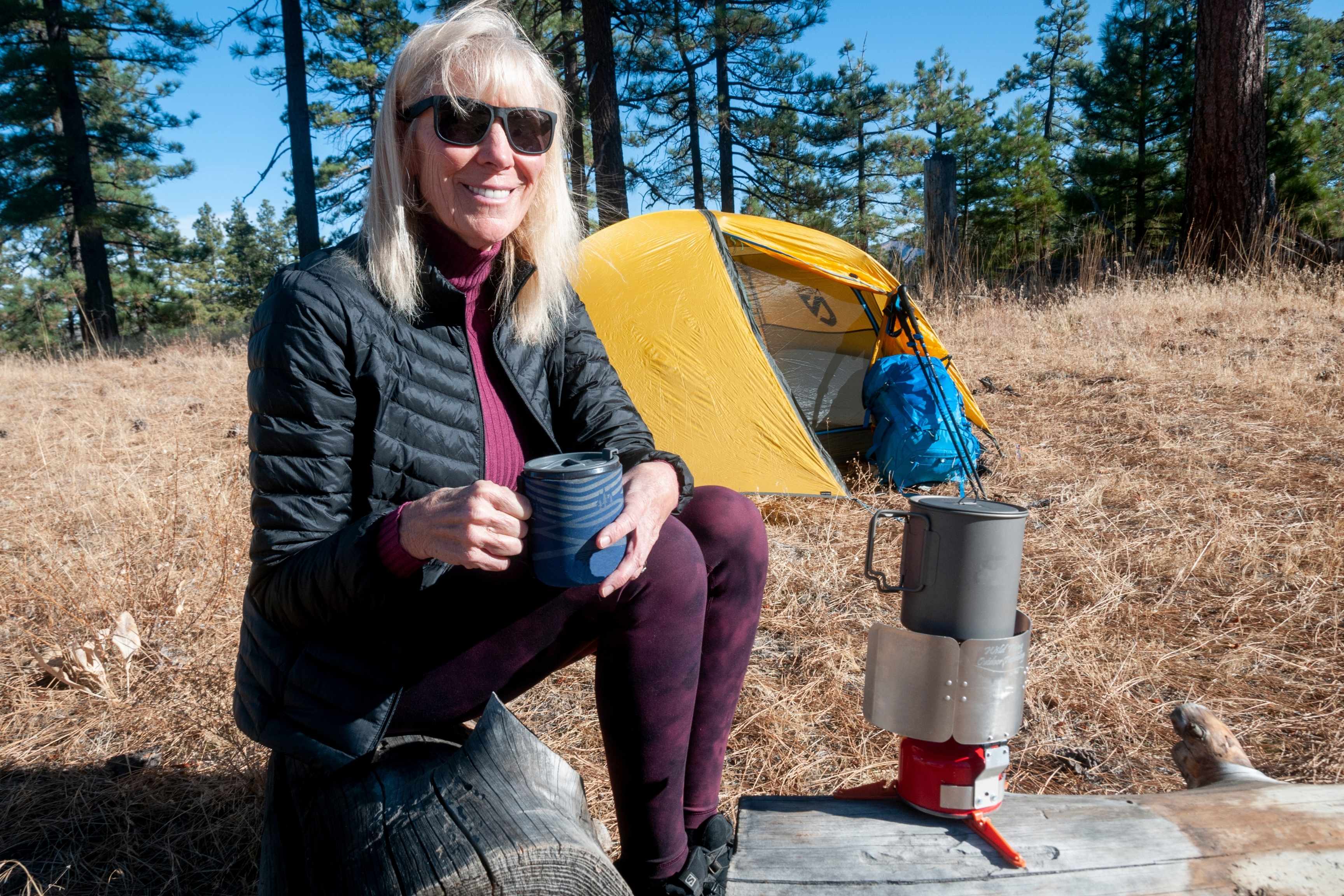 camper sits next to stove with wind screen