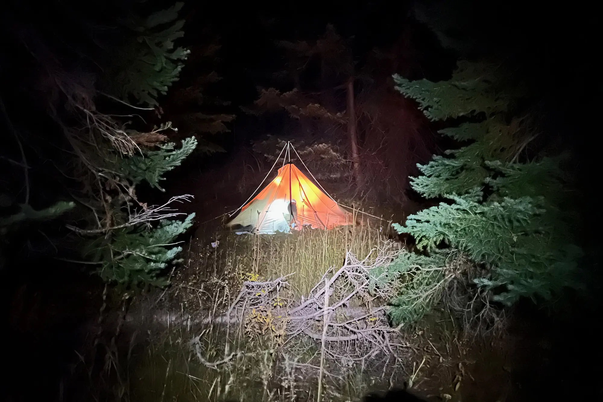 A tent glows in the darkness illuminated by a headlamp