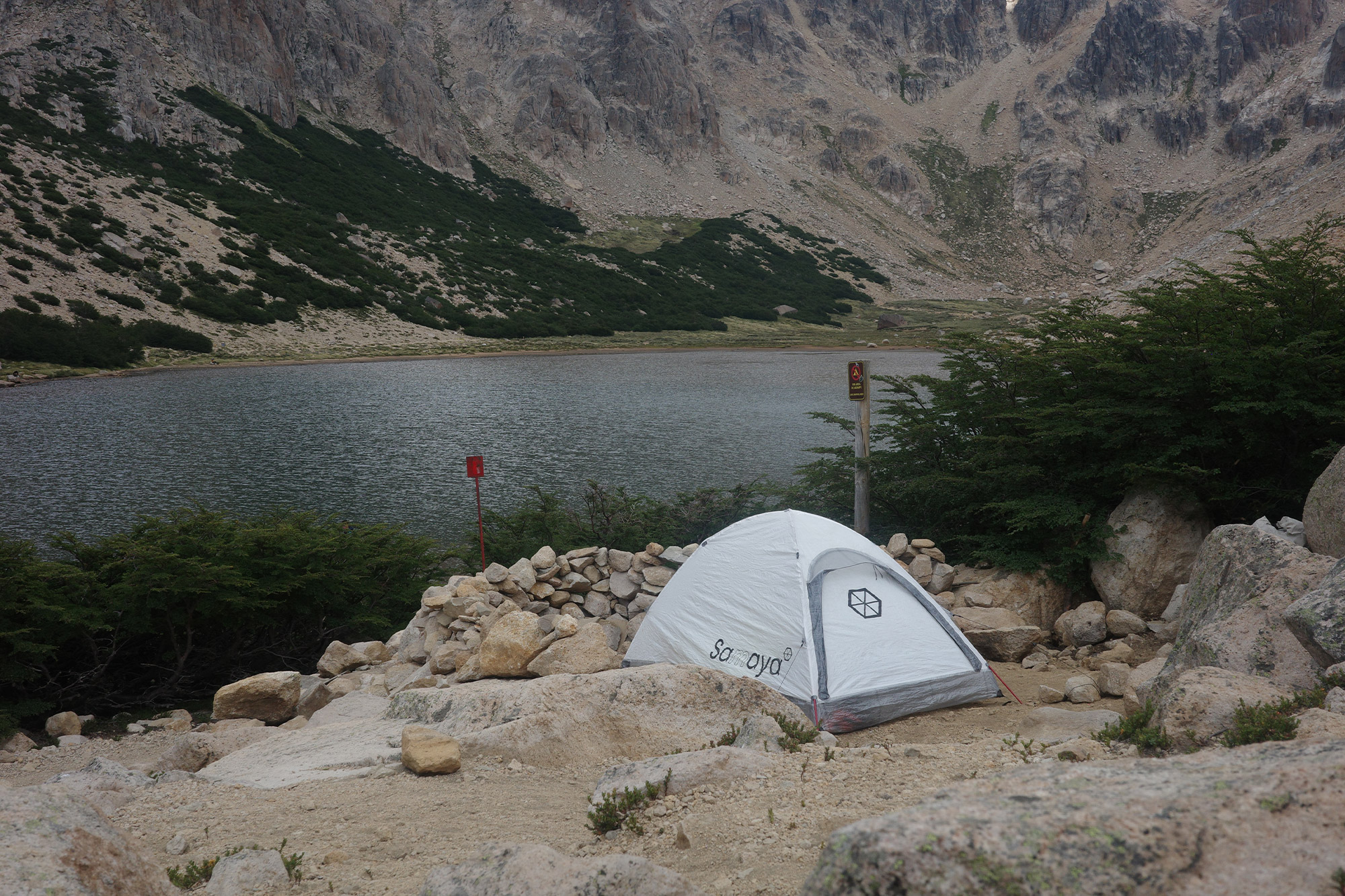Samaya tent pitched near a lake with steep rocky mountains in the background