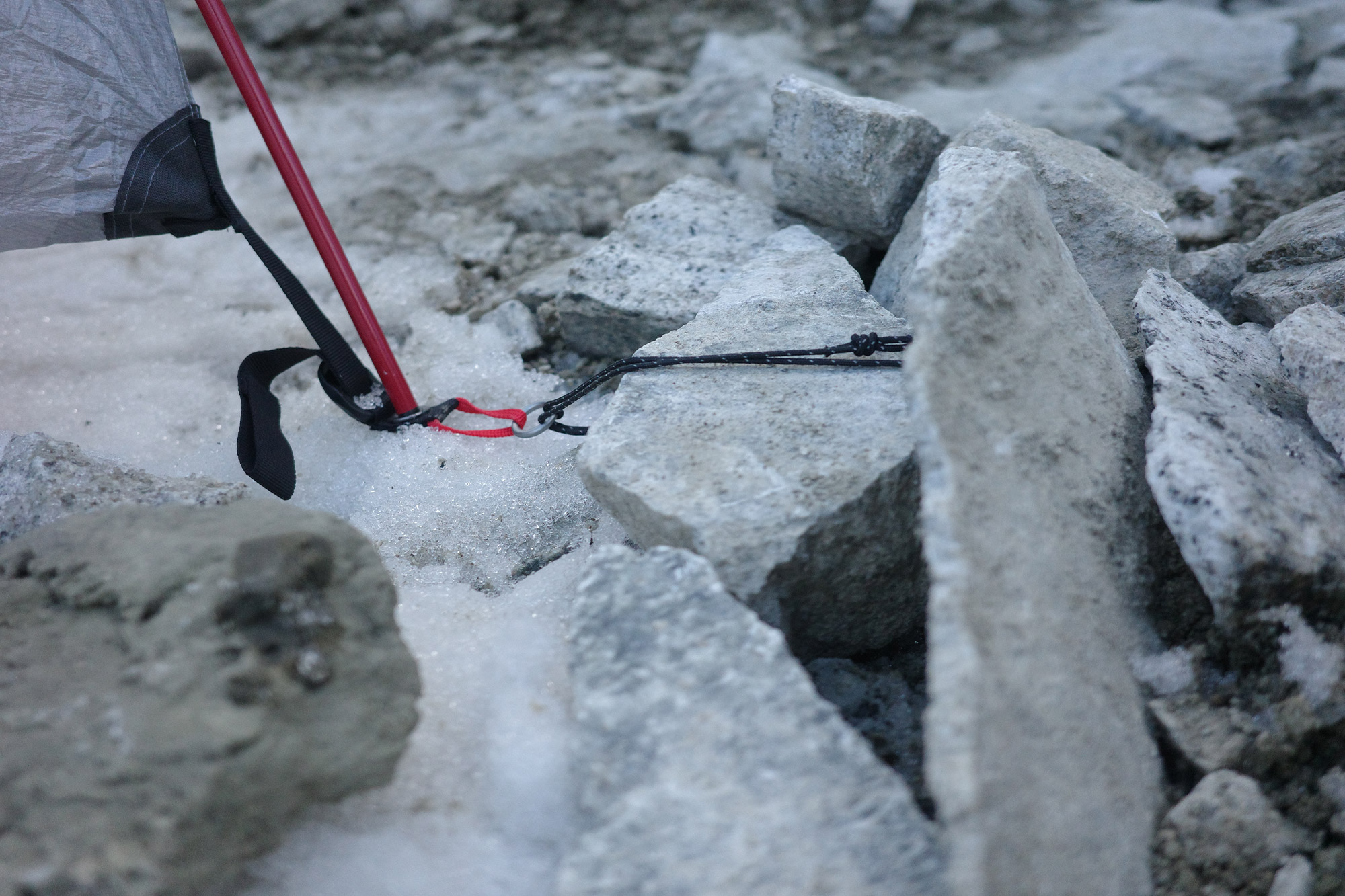 Tent guyline secured around rocks on icy ground for stability