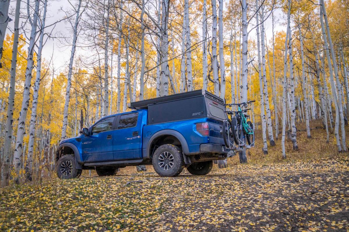 A blue pickup truck in an autumn forest carrying two bikes on a 1Up Heavy Duty bike rack