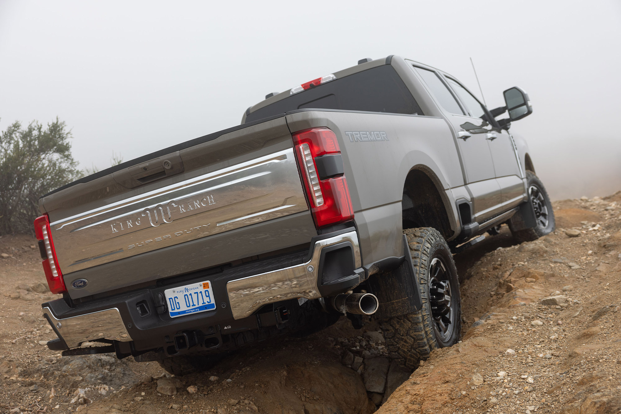 Rear view of the 2026 Ford F 350 King Ranch Tremor climbing over rocks on a dirt trail