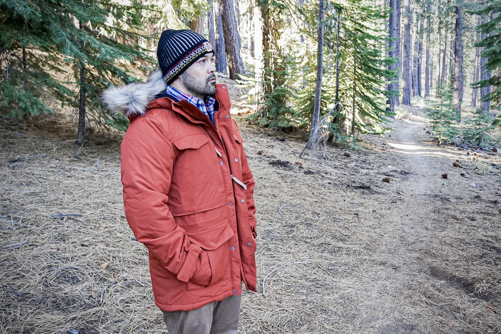 A handsome man models the Fjallraven Nuuk Parka in an orange color.