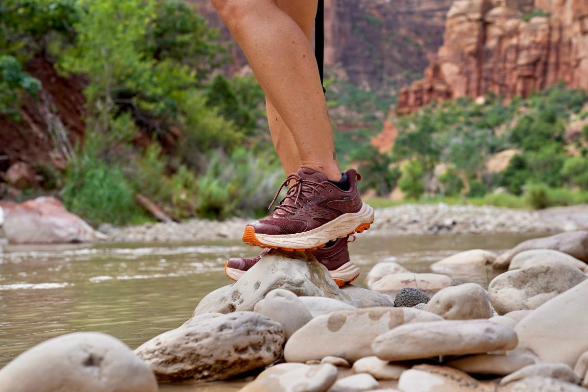 A woman stands next to a river while wearing hiking shoes