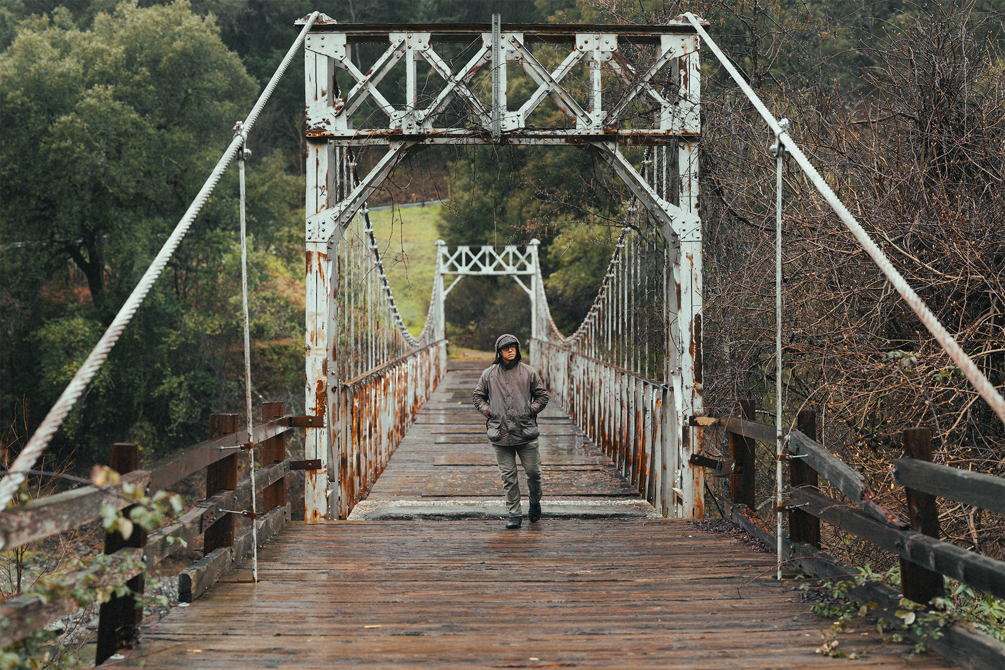 A person walks across a wet suspension bridge wearing the Barbour Beaufort Wax Jacket