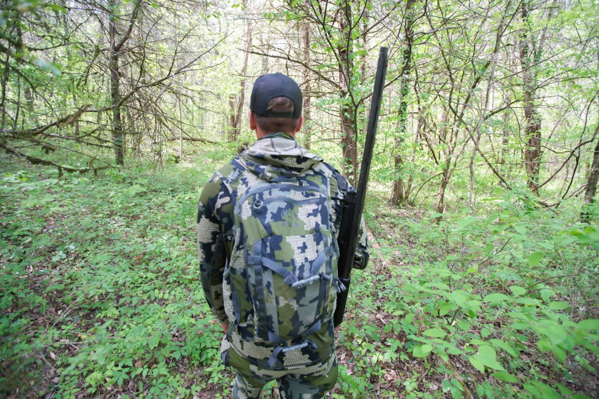 The rear view of the KUIU Rival Turkey Vest being worn by a hunter in the woods.