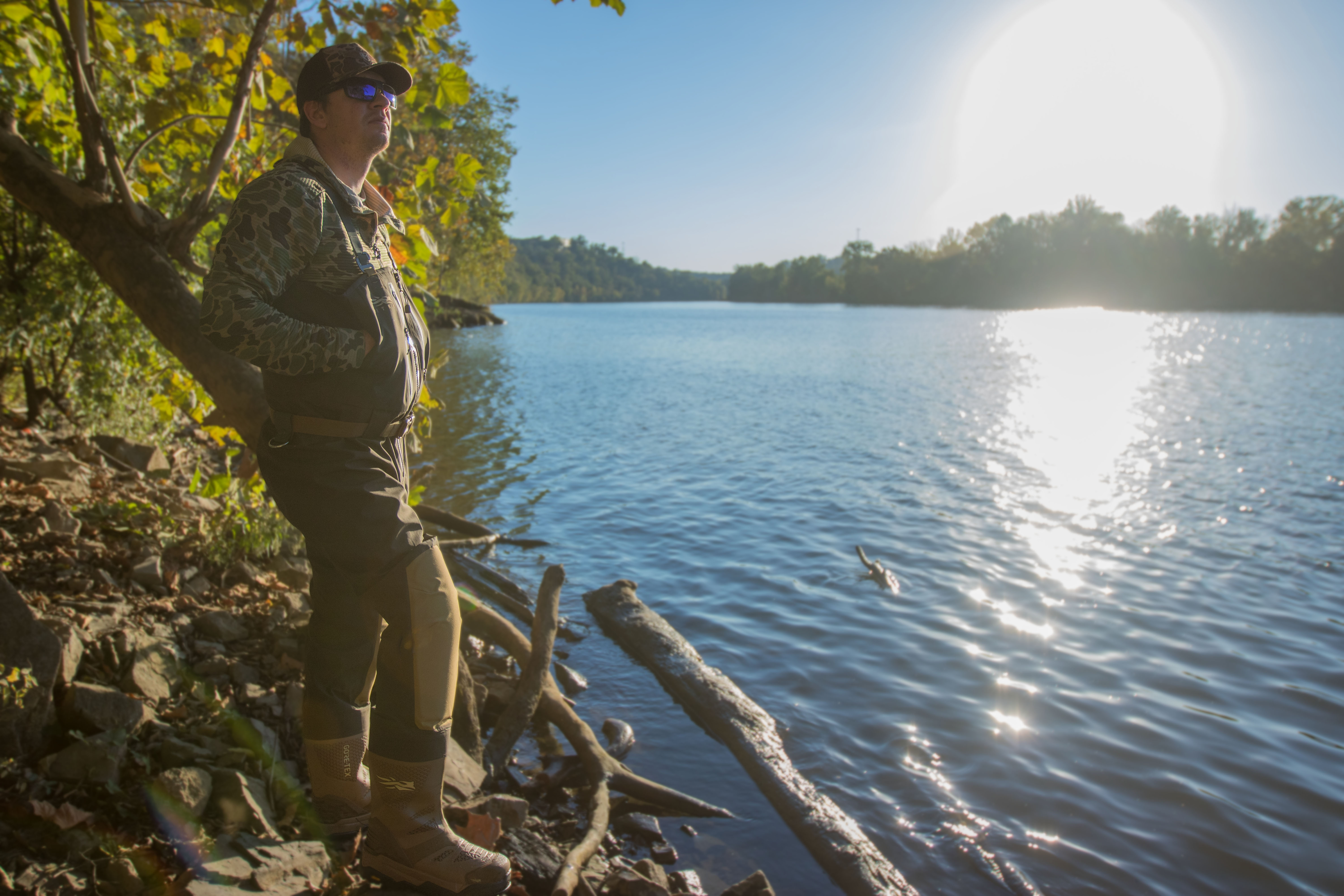 A hunter on the side of a river wearing waders
