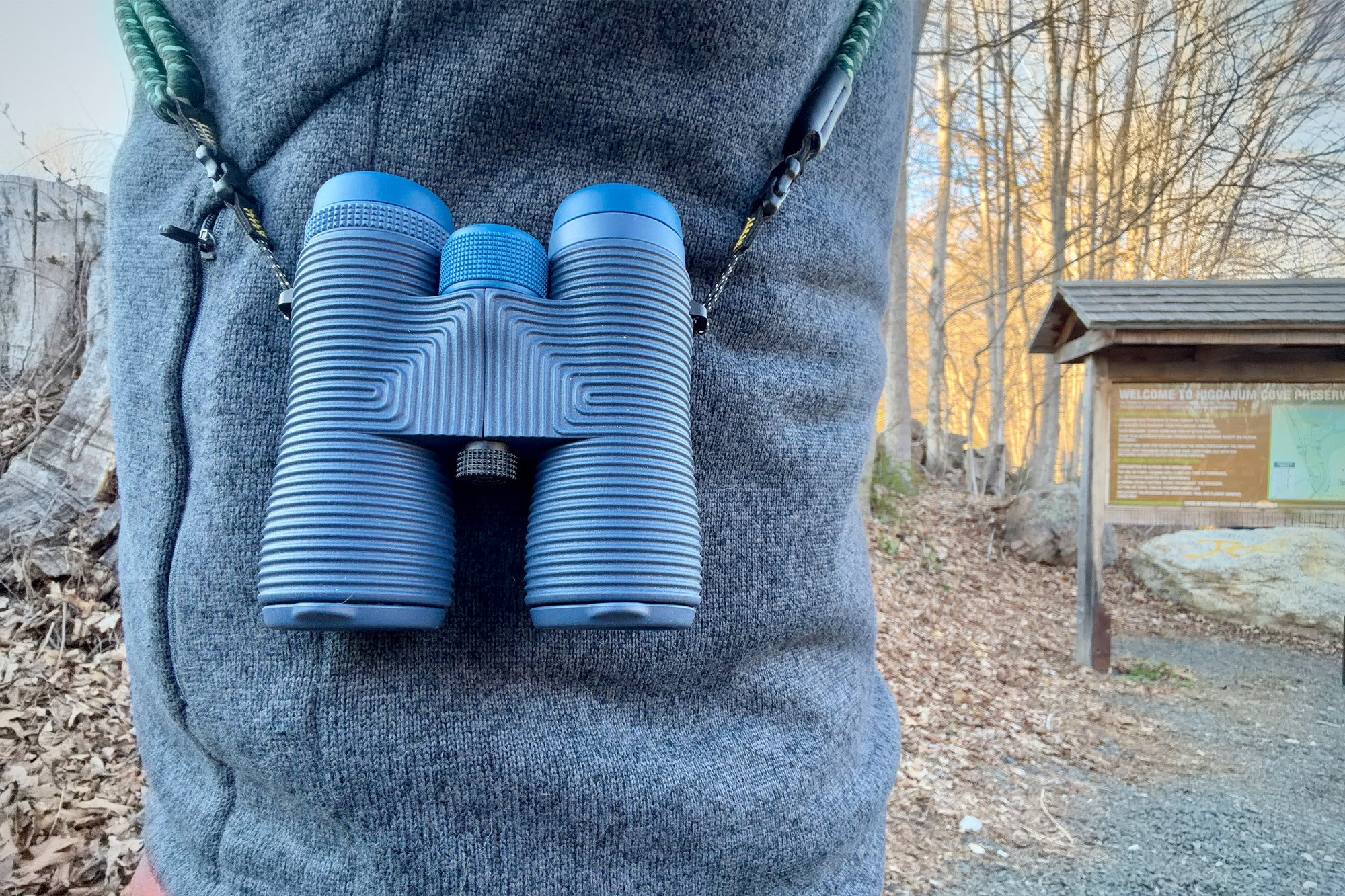 Field Issue 42 binoculars hanging from a neck strap on a jacket during a trail walk
