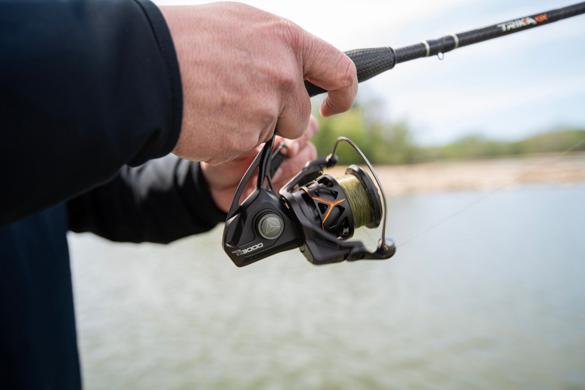 A hand on a fishing rod reeling in line with a spinning reel.