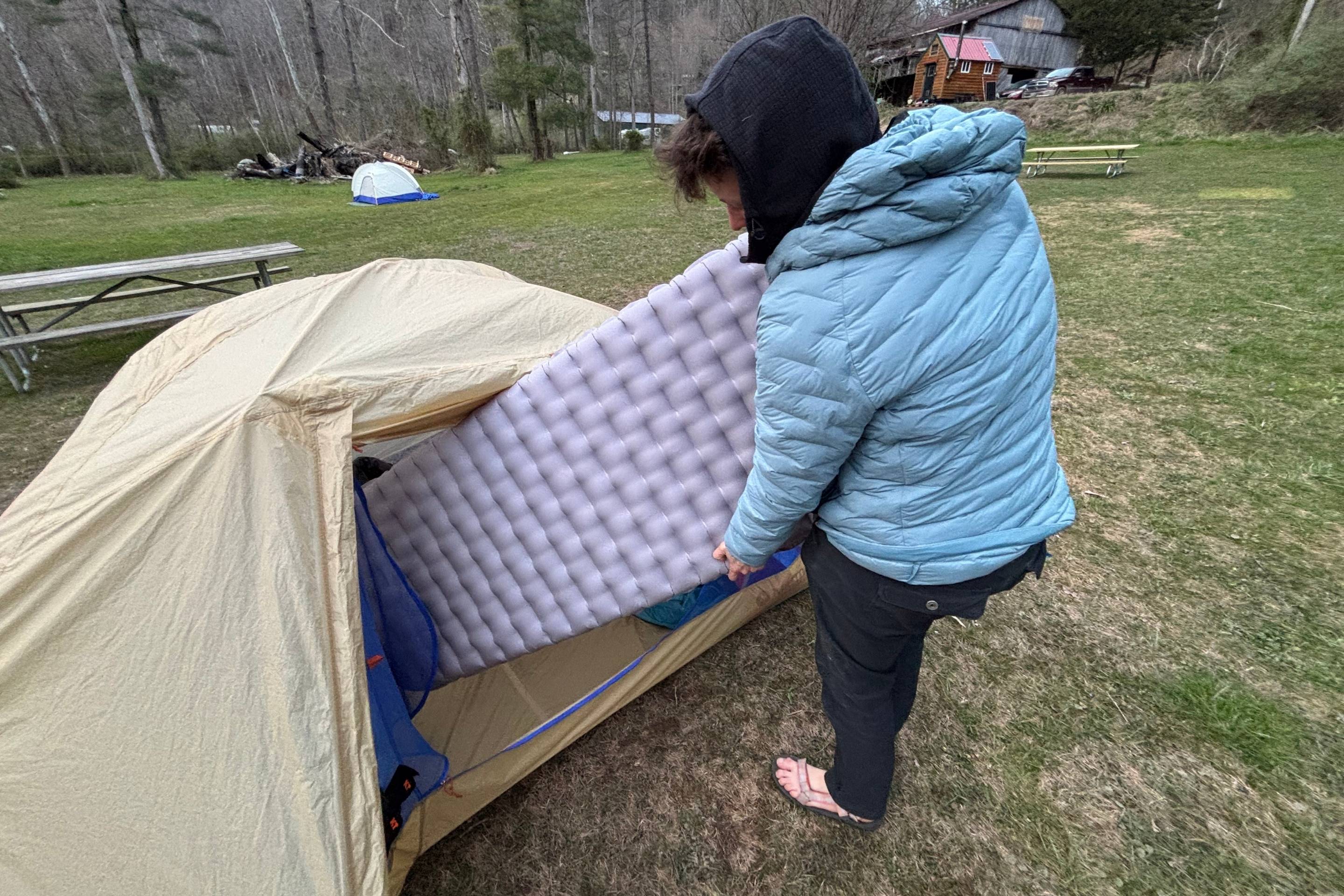 person putting gray sleeping pad into a tent