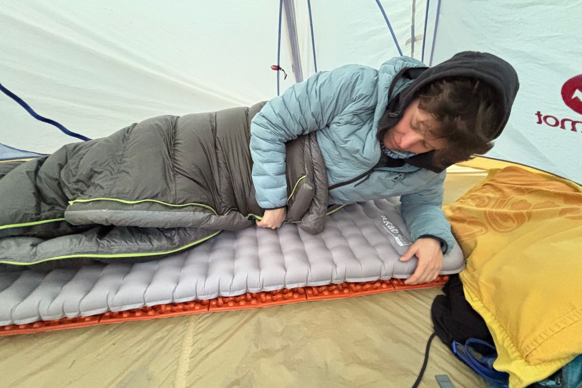 person lies on sleeping pad with sleeping bag