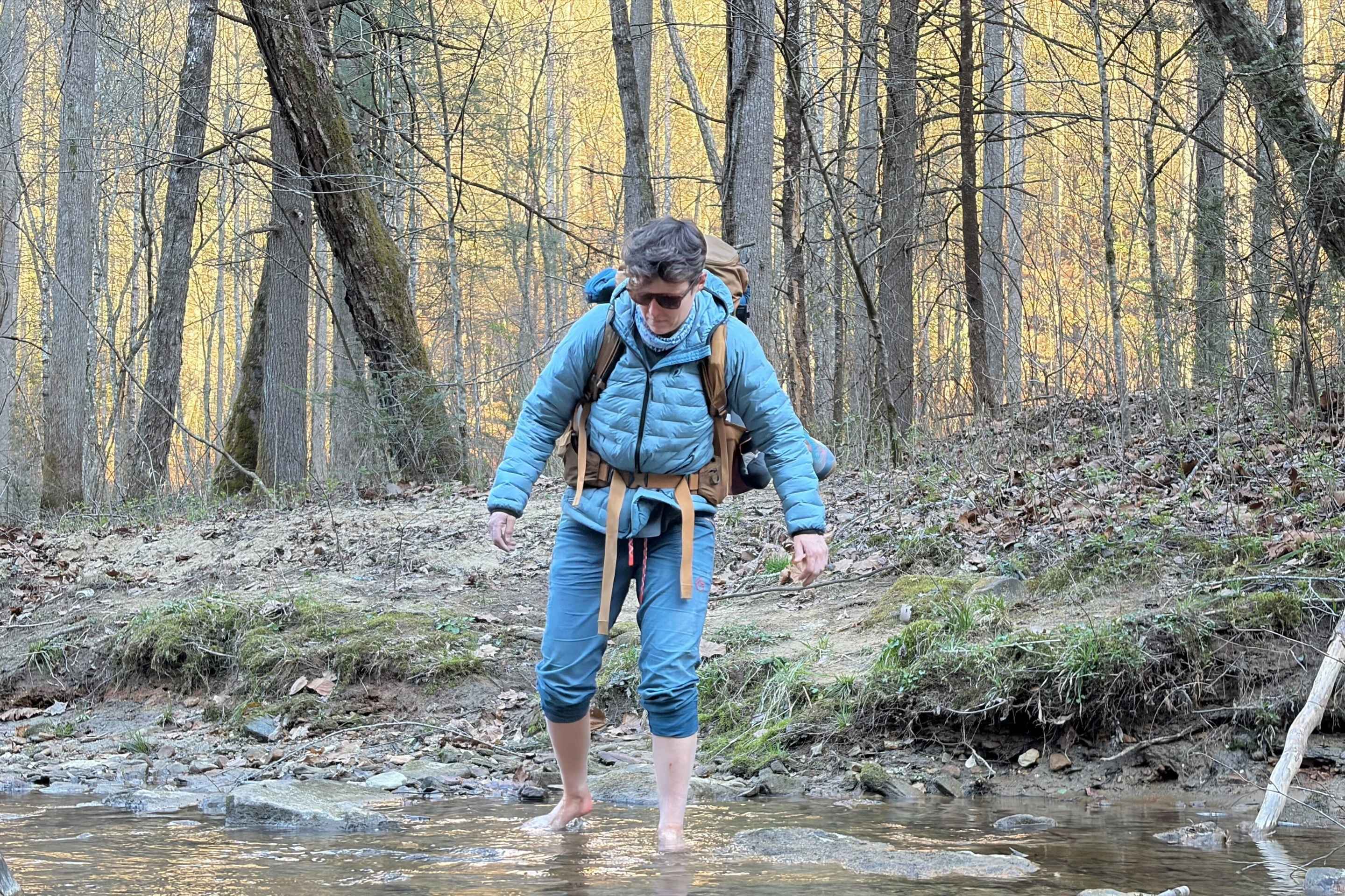 woman crosses a stream with her pants rolled up