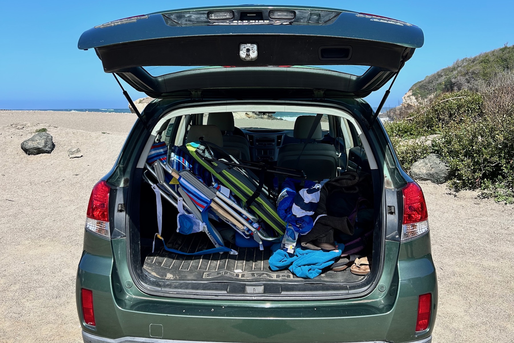 Beach umbrellas and beach chairs loaded in the back of a car that's parked at the beach