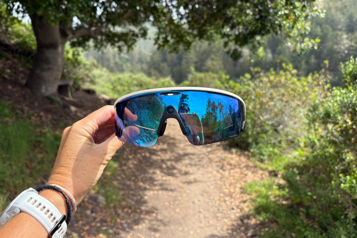 Hand holding Oakley Meta Vanguard glasses on a forest trail