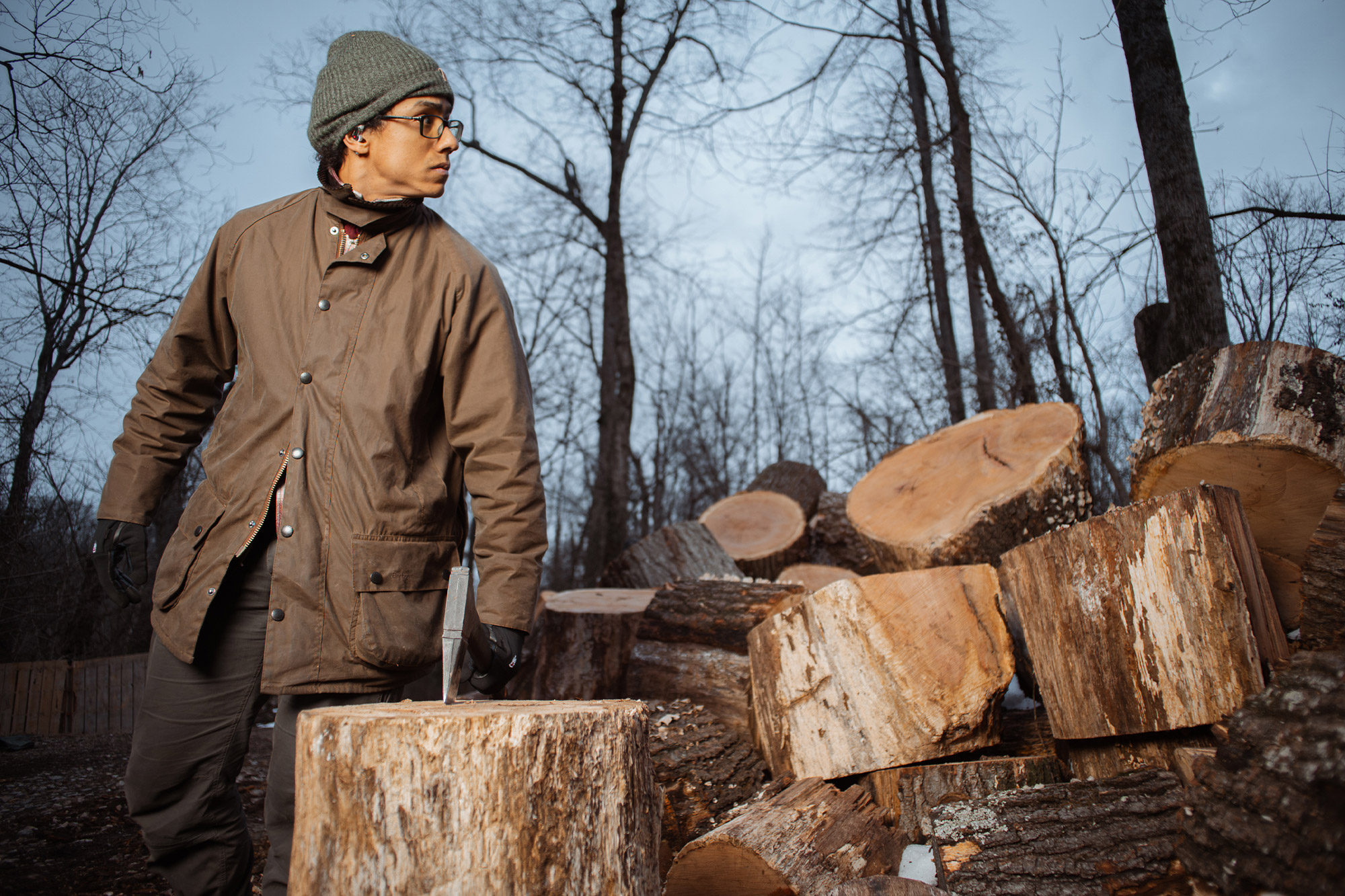 person wearing Barbour Beaufort jacket by the chopped woods